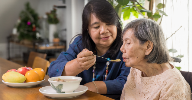 Caregiver helping an older adult with a serving of food.