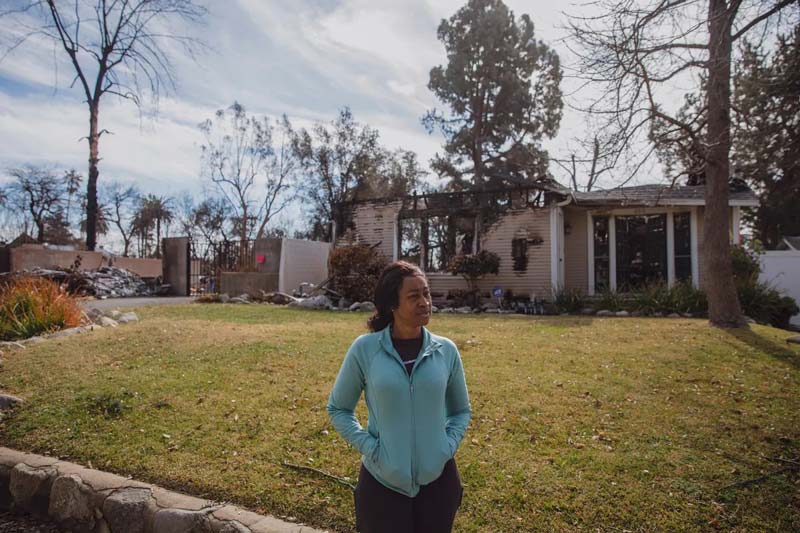 Woman stands in front of destroyed house.